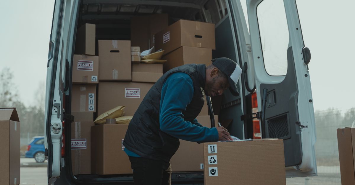Delivery man sorting packages in van, organizing shipments for distribution.