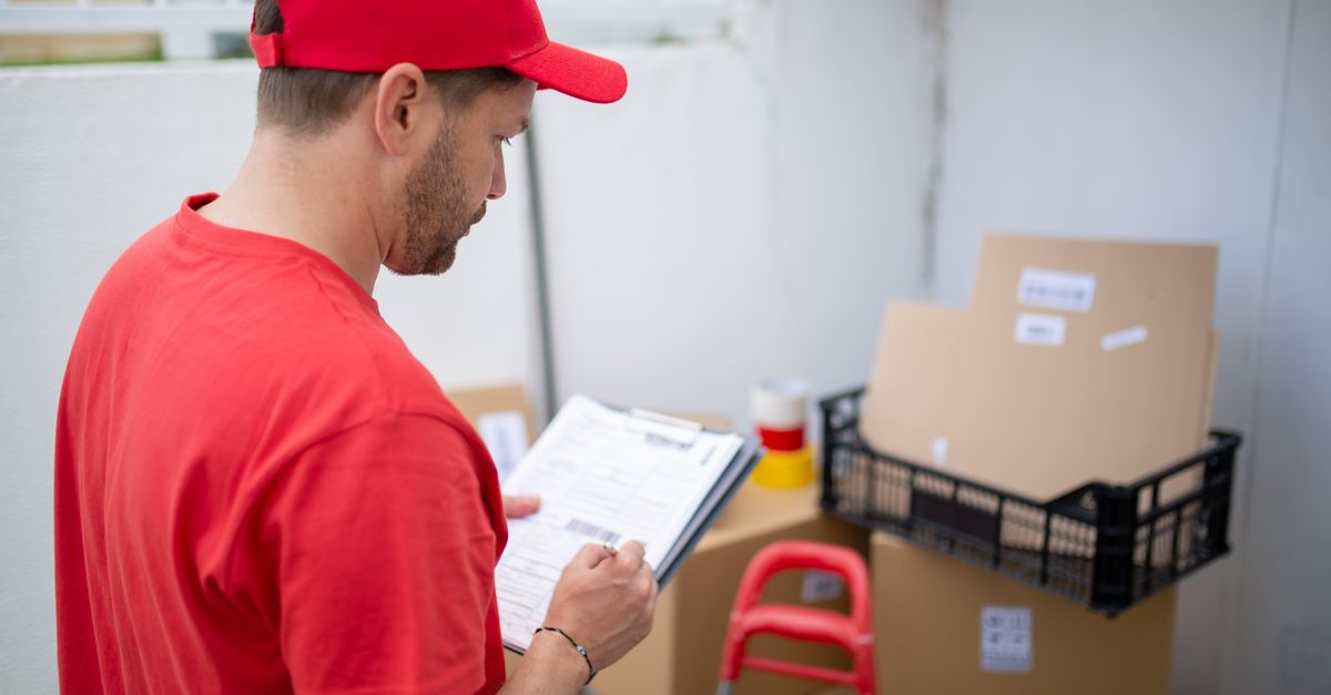 Delivery person in red uniform checks packages. Outdoor location, Portugal.